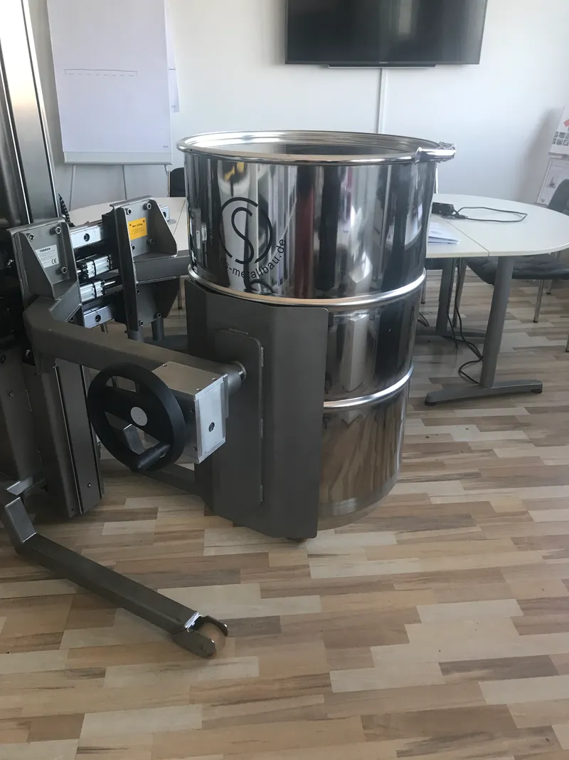 Mobile lifting aid ezzLIFT with a gripper holding a stainless steel drum.