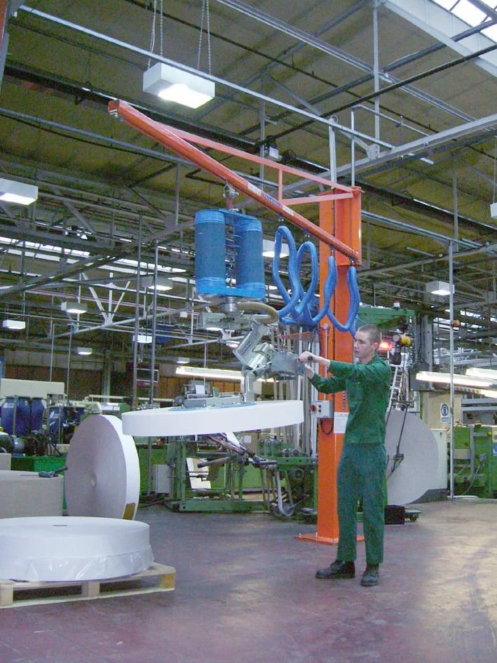 Handling system picking up a large material roll in a production hall.