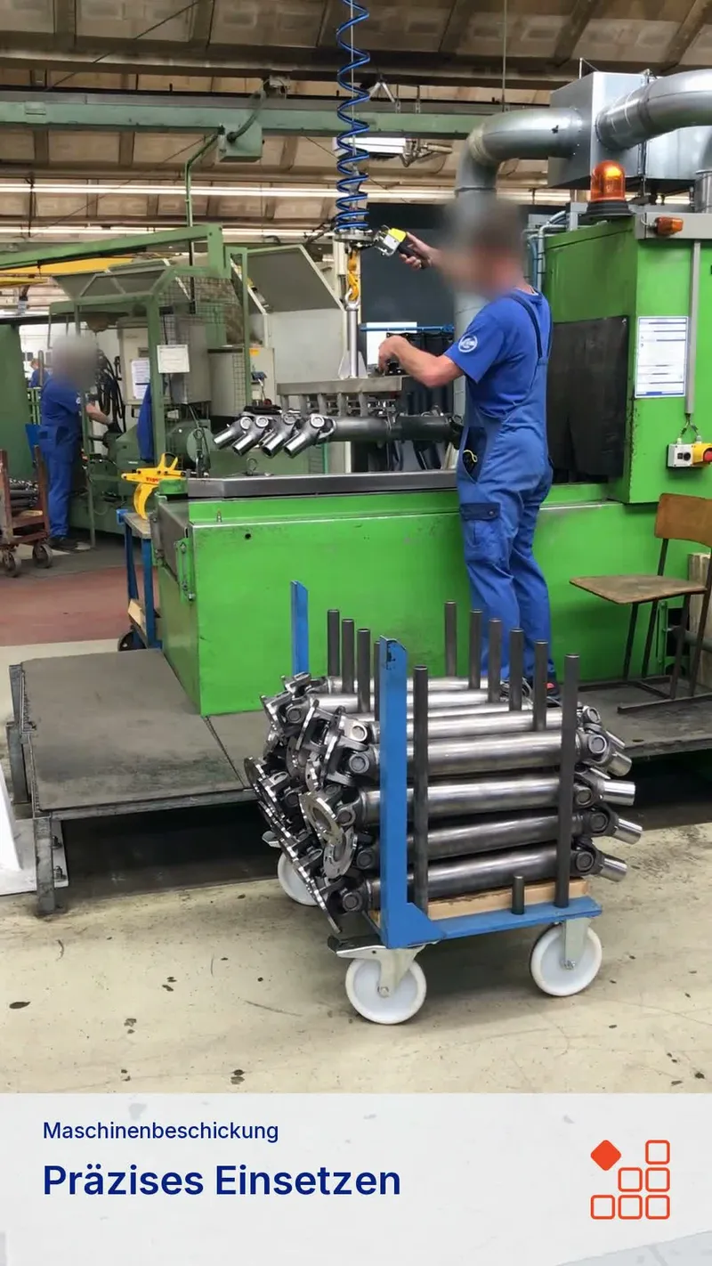 Multi-part gripper transferring drive shafts from a trolley into a machining station.